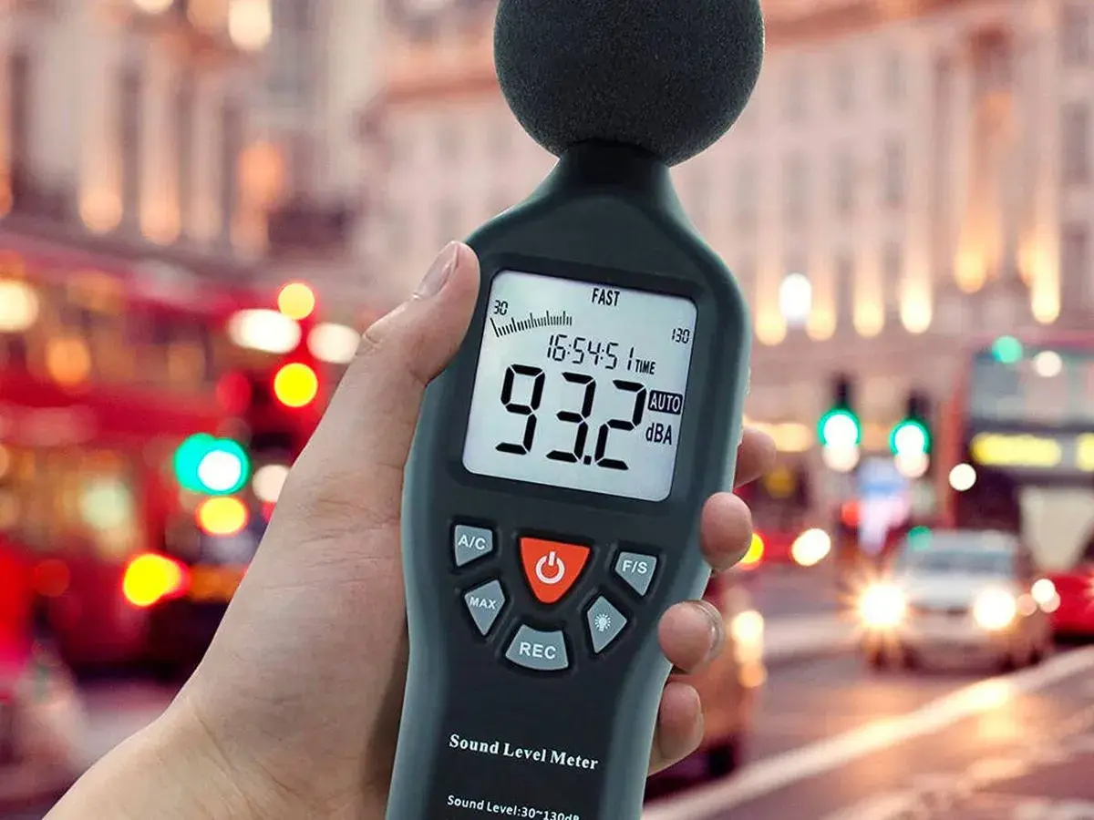 Mano sosteniendo un medidor de sonido para medir db en una calle ruidosa de la ciudad.
