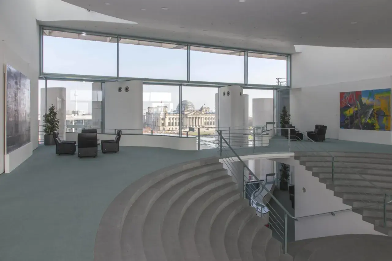 Modernes Foyer im Bundeskanzleramt mit Blick auf das Reichstagsgebäude. Sitzgruppen und eine geschwungene Treppe laden zum Verweilen ein.