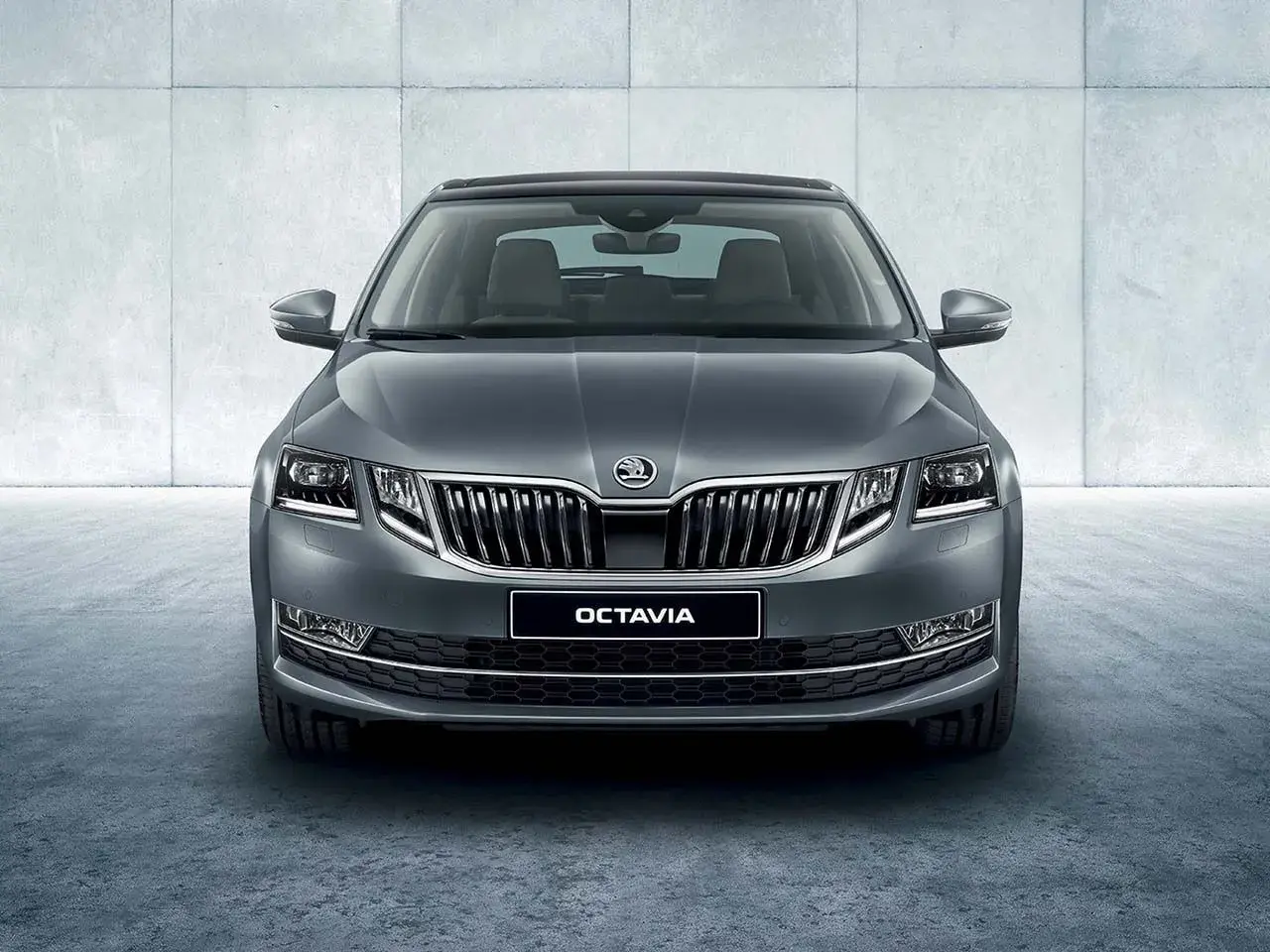 Szary Skoda Octavia sedan z chromowanym grillem i światłami LED, prezentujący się elegancko na tle betonowej ściany.