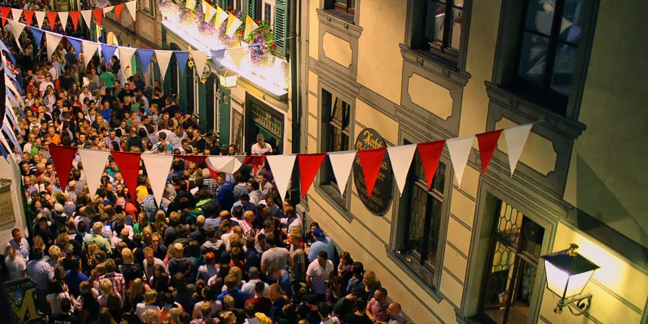Buntes Treiben beim Bamberger Volksfest. Girlanden schmücken die Gasse, Menschenmassen feiern ausgelassen.