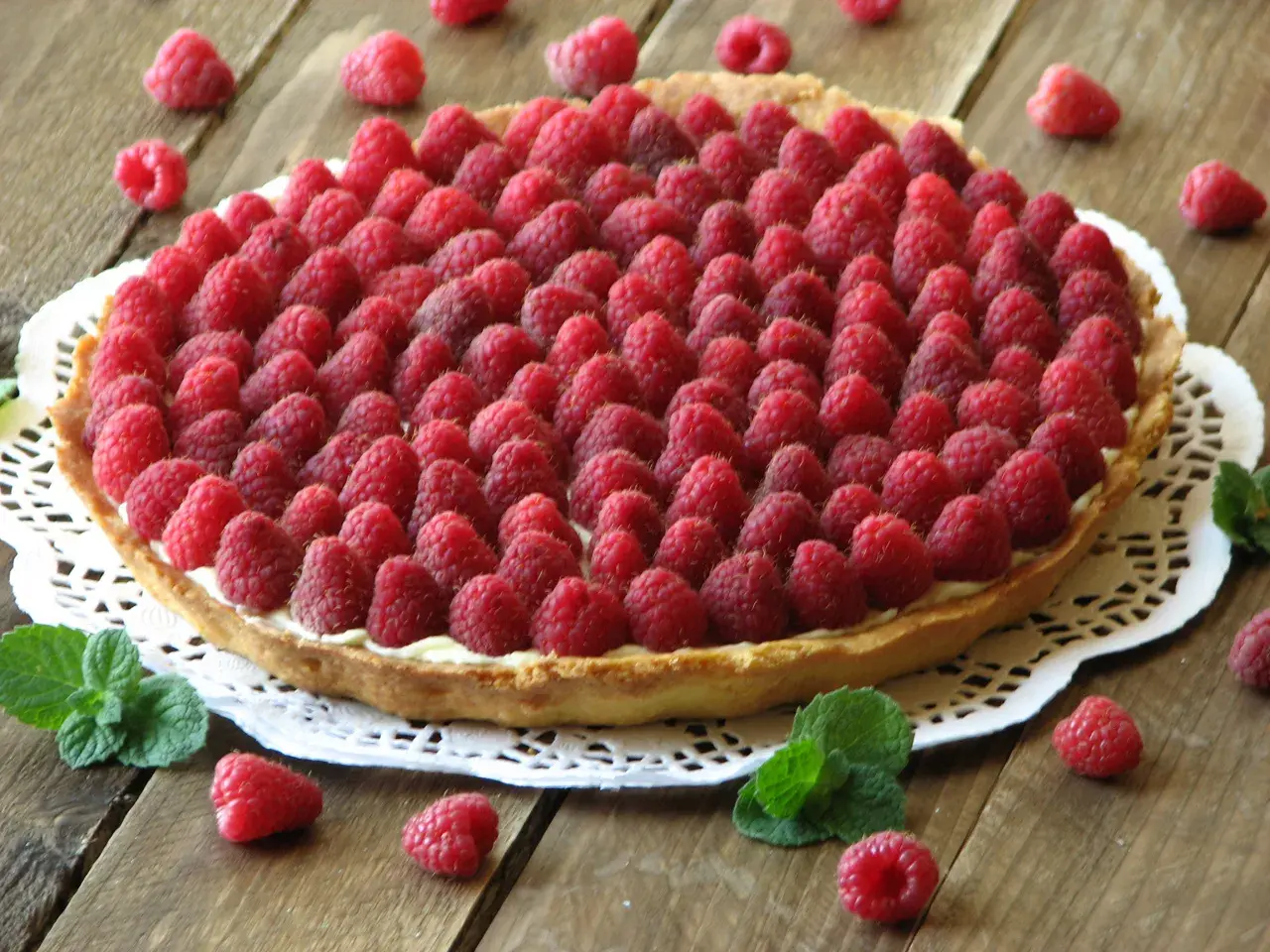 Pyszna tarta z malinami, udekorowana świeżymi listkami mięty. Idealna na letnie popołudnie.