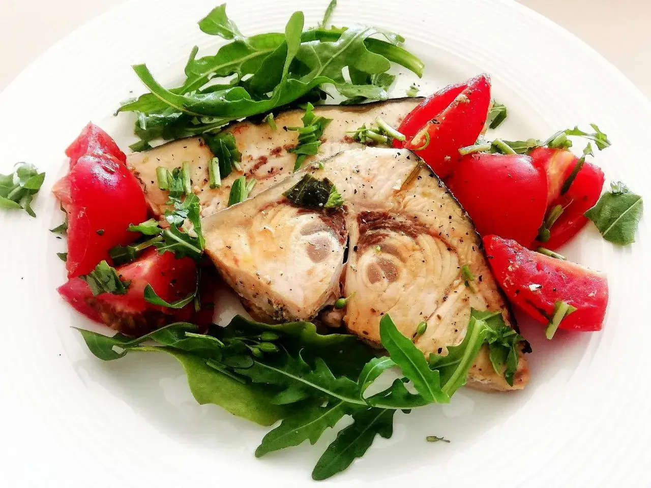 Spiedini di pesce spada in padella con pomodorini freschi e rucola, un piatto leggero e saporito.