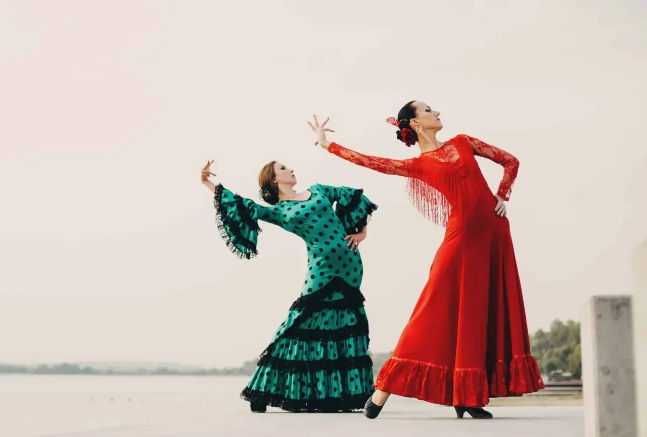 Dos mujeres bailan flamenco. Una con vestido verde de lunares, la otra con rojo. Inspiración para palos del flamenco para niños.