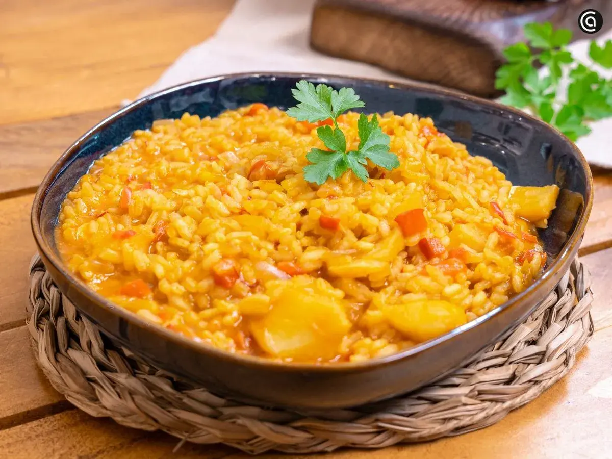 Un plato humeante de arroz con bacalao, adornado con perejil fresco, servido en un cuenco azul sobre una esterilla de mimbre.