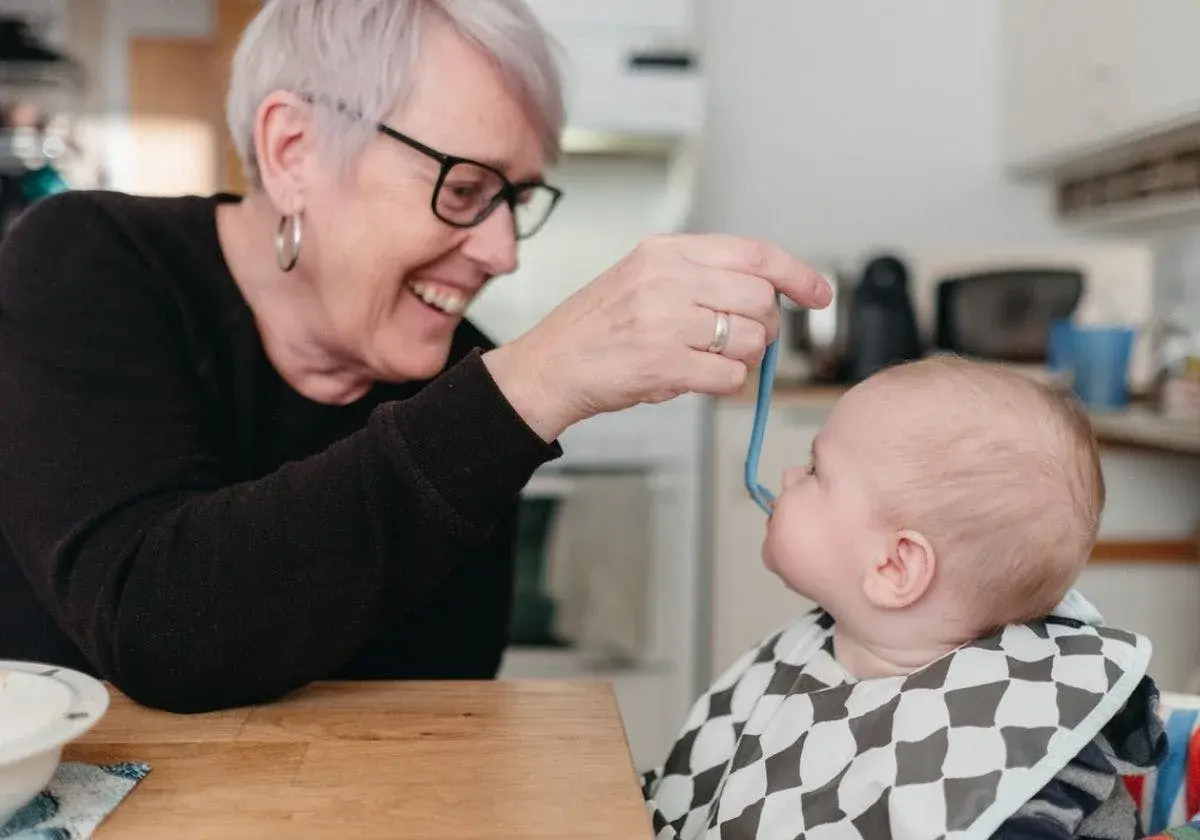 Glad mormor matar bebis med smakportioner. Första maten för en 4 månader gammal bebis.
