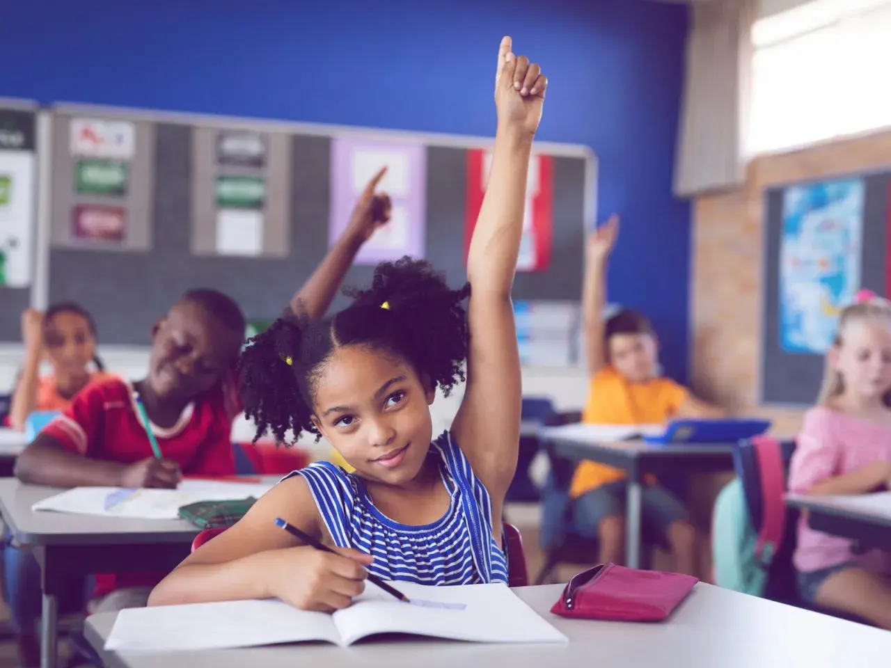 Ein Mädchen hebt im Unterricht die Hand. Viele Kinder lernen, was die bilingualer unterricht vorteile nachteile mit sich bringt.