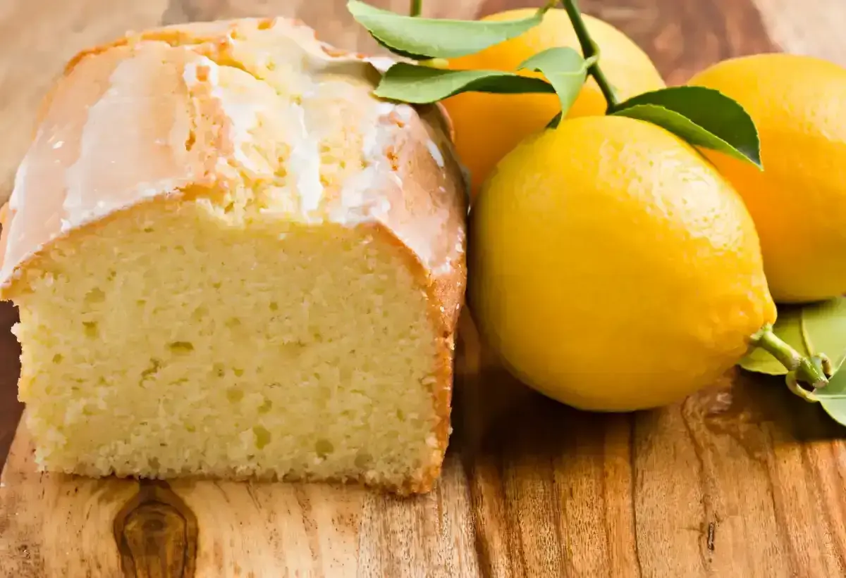 Un délicieux gâteau citron, avec un glaçage blanc et des citrons frais sur une planche en bois.