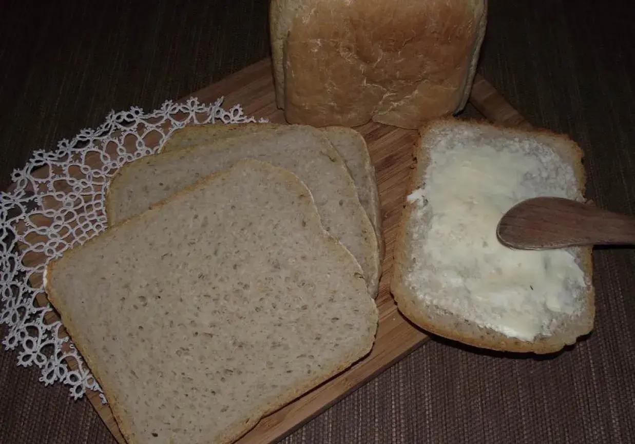 Chleb pszenno żytni na zakwasie, pokrojony w kromki. Jedna kromka posmarowana masłem, obok leżą kolejne.