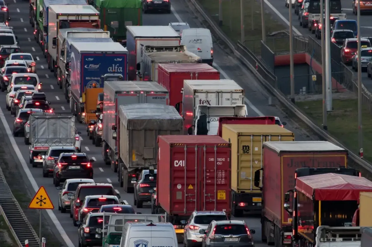 Korki na autostradzie w Polsce. Długi sznur samochodów i ciężarówek, widoczne znaki ostrzegawcze.