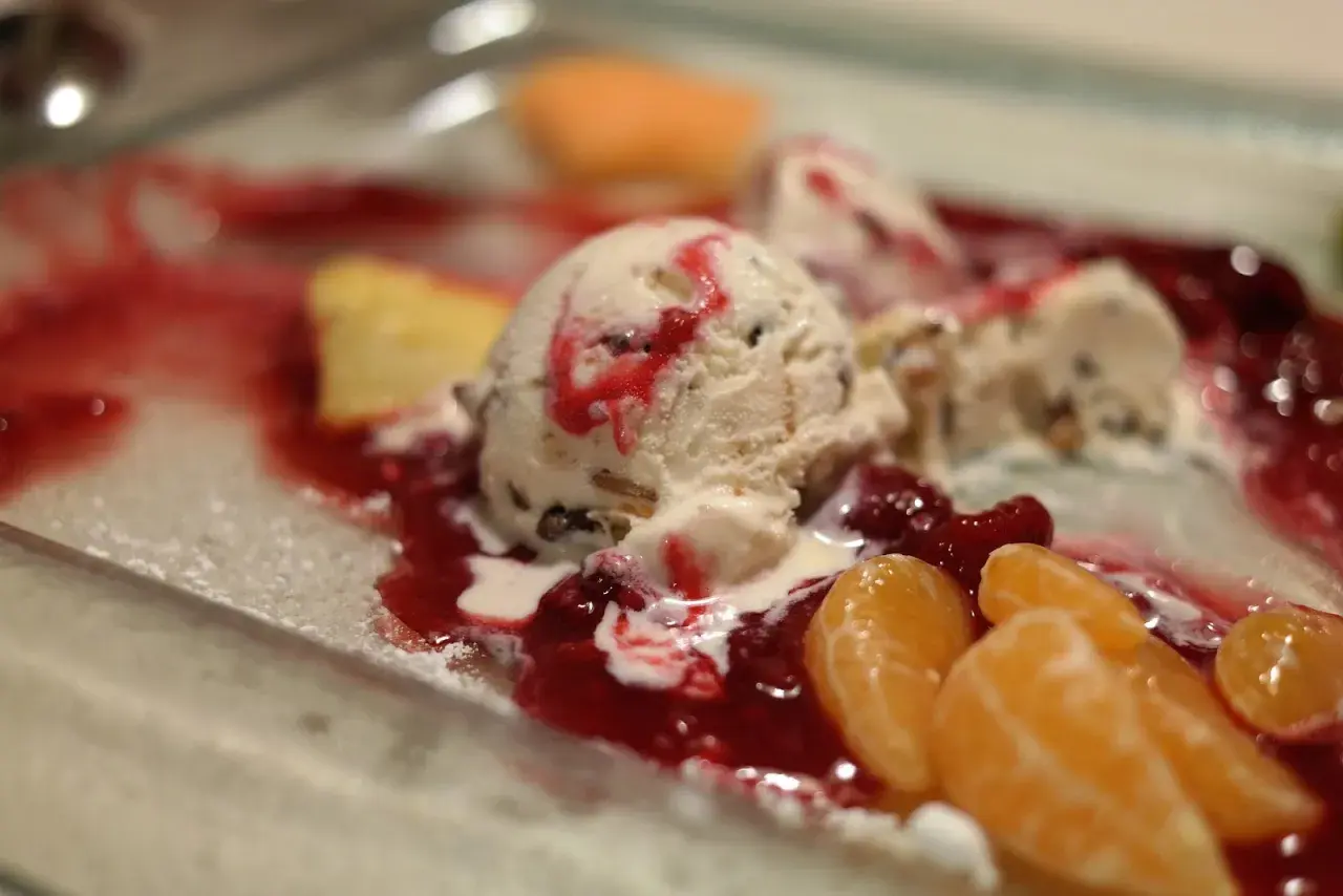 Cremiges Mascarpone Eis mit roter Fruchtsauce und Mandarinenstücken auf einem Teller.