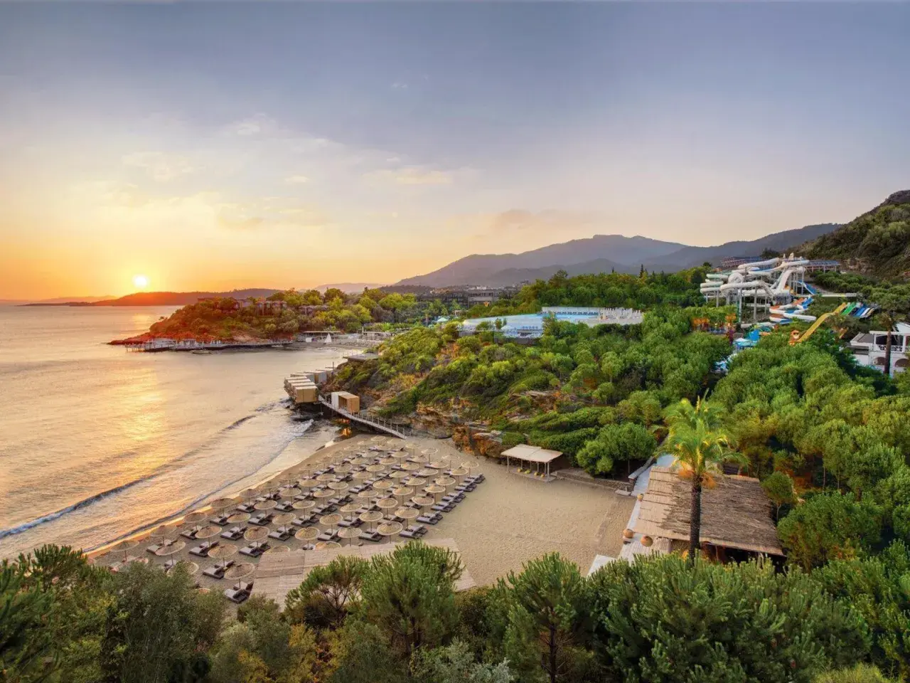 Sonnenuntergang am Club Marvy: Ein Strand mit vielen Liegen, ein Wasserpark und üppige Vegetation.
