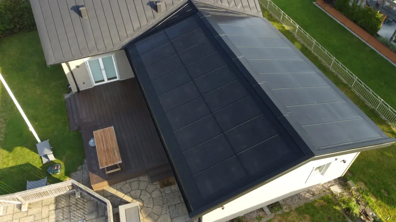 Tak med svensktillverkade solceller som täcker en stor del av takytan. Ett modernt hus med trädäck och grönskande trädgård.