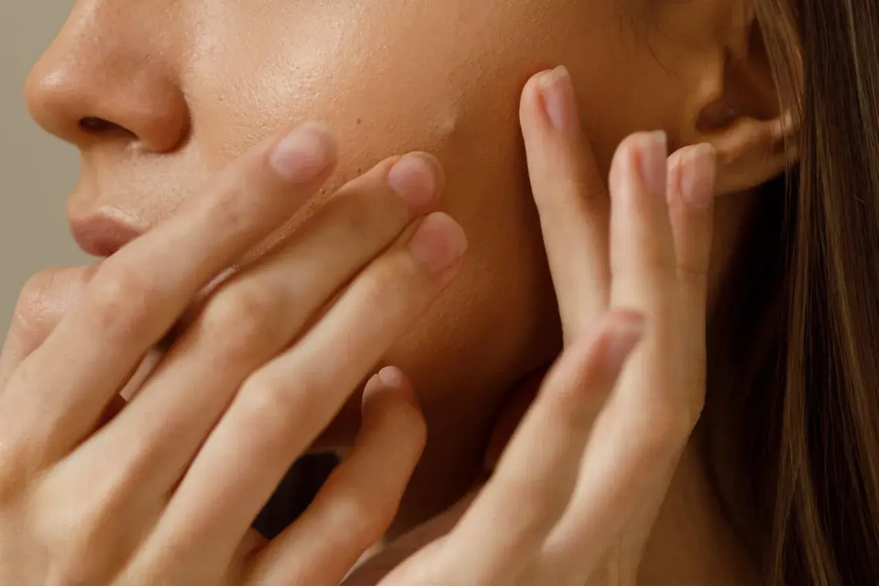 Gros plan sur une peau claire avec un petit bouton sur le visage, touché par des doigts délicats.