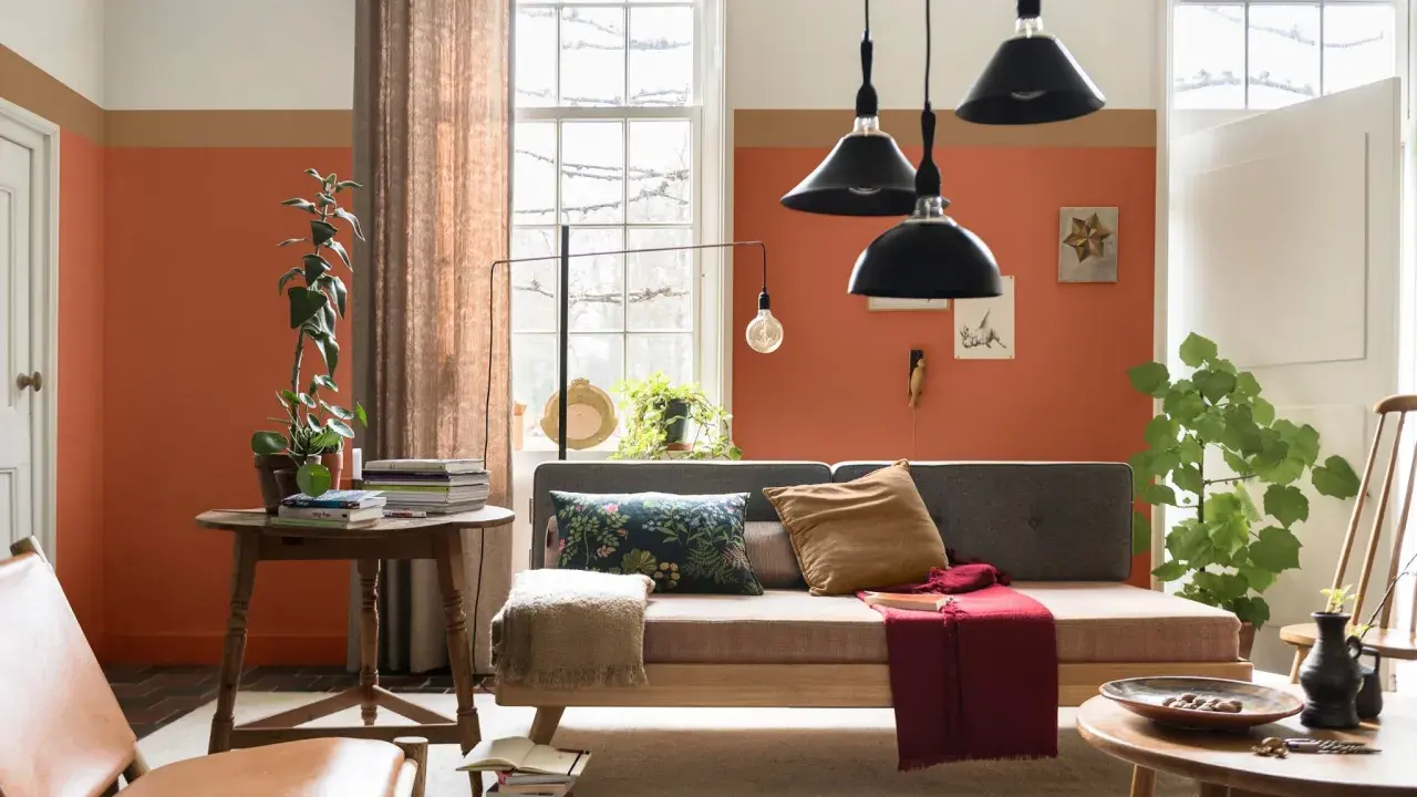 Wohnzimmer mit orangefarbenen Wänden, die mit abriebfester Farbe gestrichen sind. Ein Sofa, ein Tisch mit Büchern und Pflanzen.