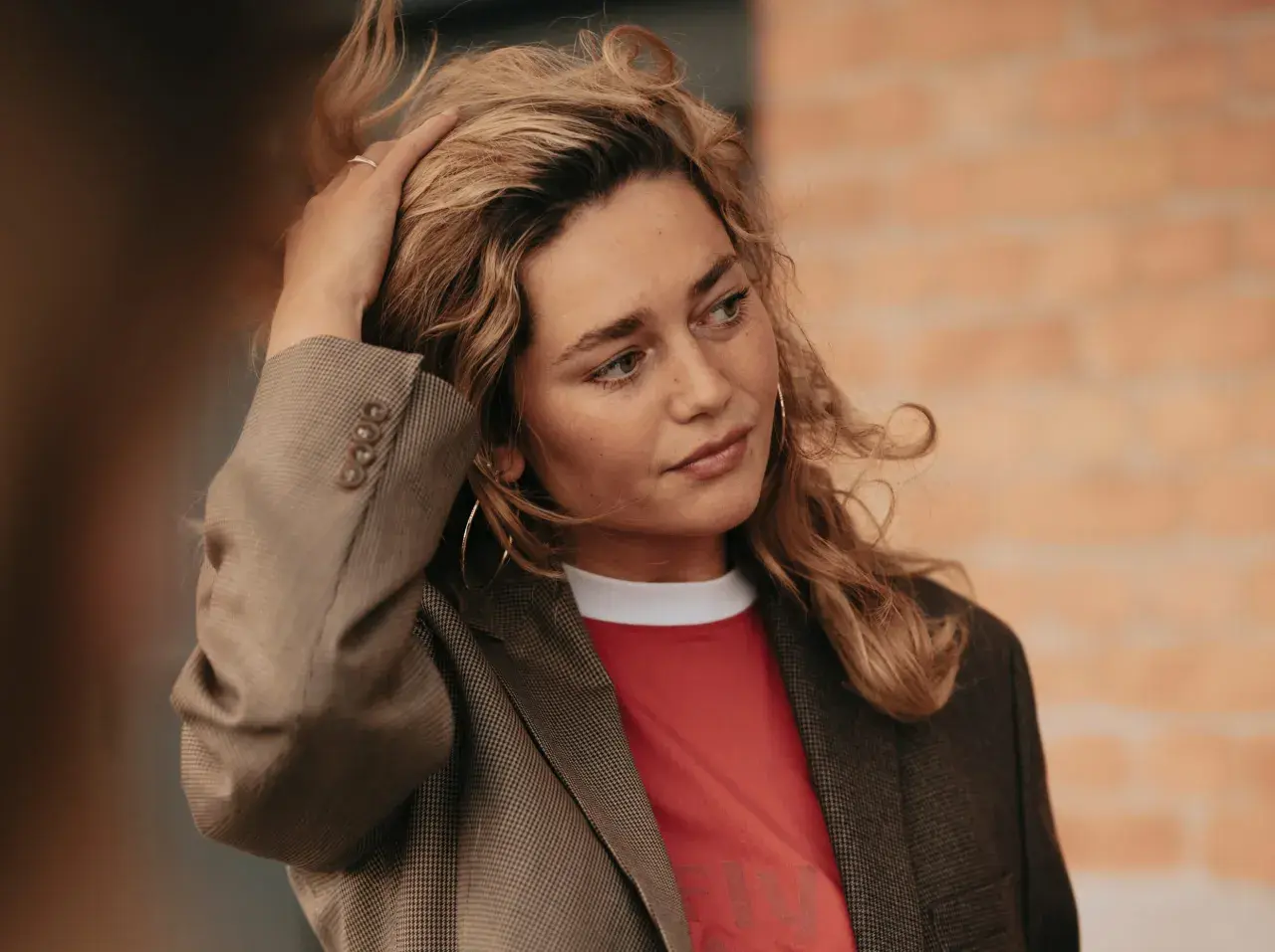 Kobieta z blond włosami w marynarce i czerwonej koszulce, dotykająca włosów.