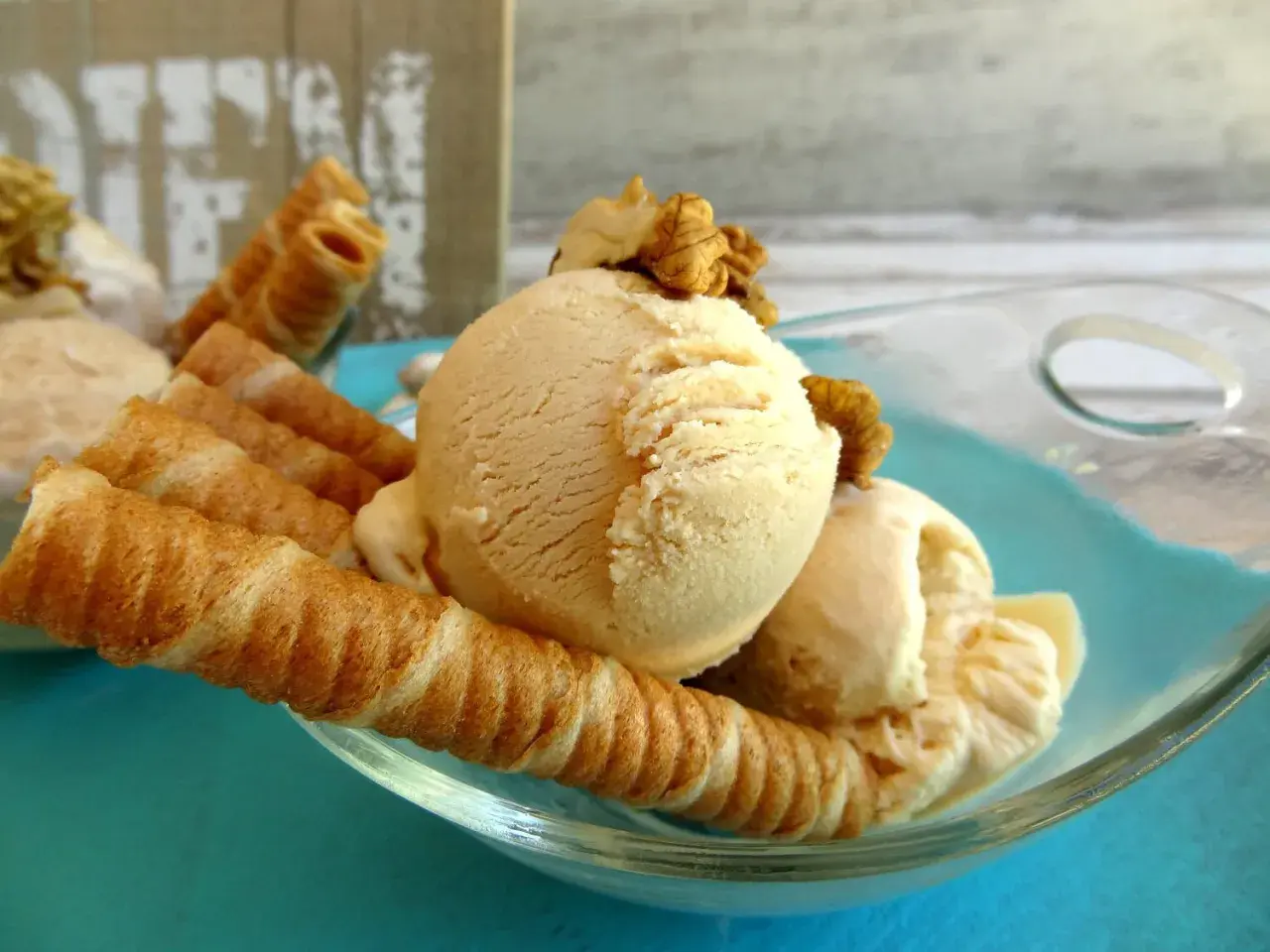 Delicioso helado de dulce de leche con barquillos crujientes y nueces, servido en un cuenco de vidrio sobre un plato turquesa.