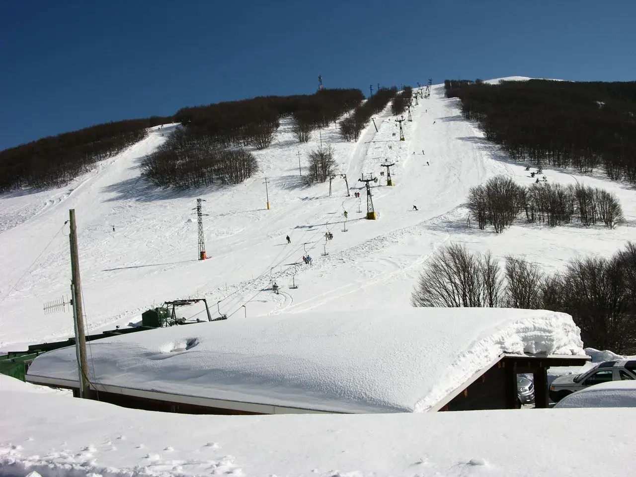 Piste innevate e skilift attivi sul monte Piselli, stazione sciistica con alberi spogli e cielo azzurro.