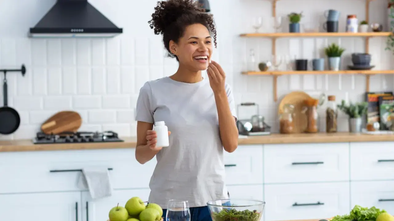 Mujer sonriente en cocina, tomando suplemento. El zinc para que sirve en la mujer es clave para su bienestar general y salud.