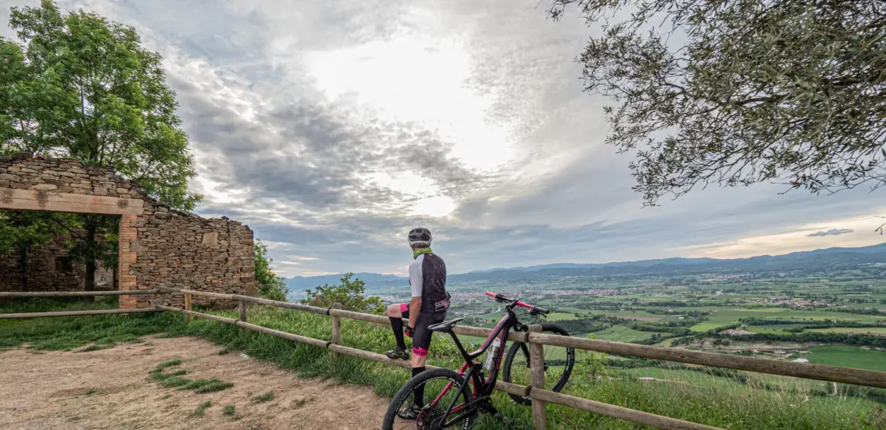 Ciclista descansa junto a su bici en ruinas de coll sa cabra, contemplando el valle.
