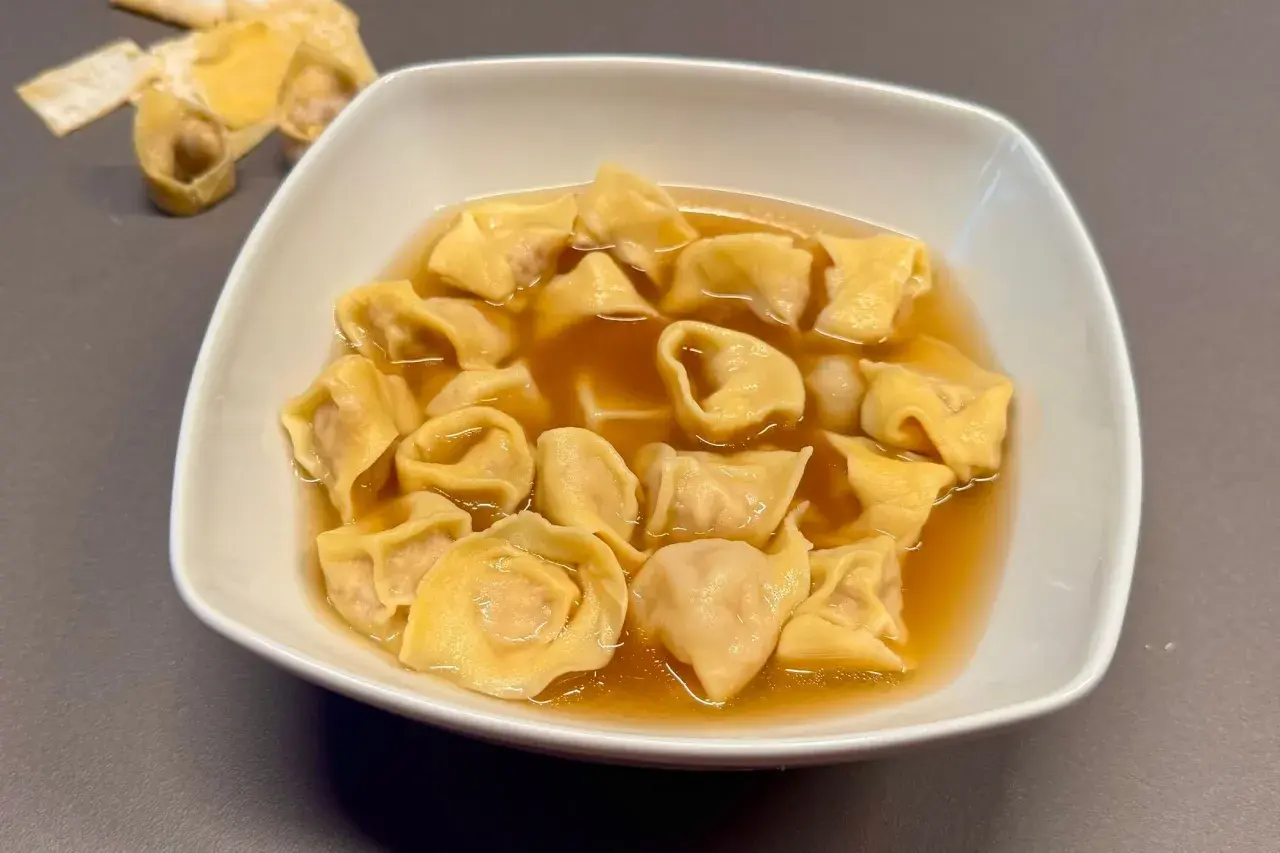 Un piatto fumante di tortellini in brodo, un classico confortante. Sullo sfondo, alcuni tortellini crudi e sfoglia.