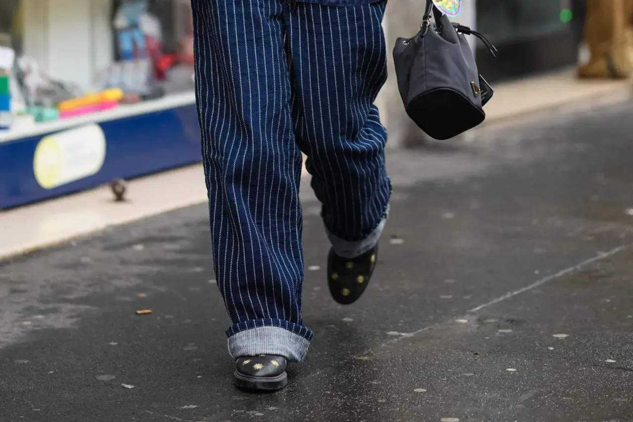 Person mit gestreiften Hosen, die die Jeans umschlagen. Schwarze Schuhe mit Sternenapplikationen und eine kleine Tasche.