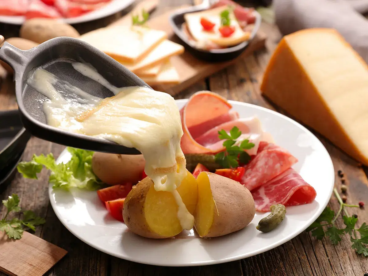 Le fromage à raclette fond sur des pommes de terre, prêt à être dégusté avec charcuterie et cornichons. Le temps de cuisson pomme de terre raclette est parfait.