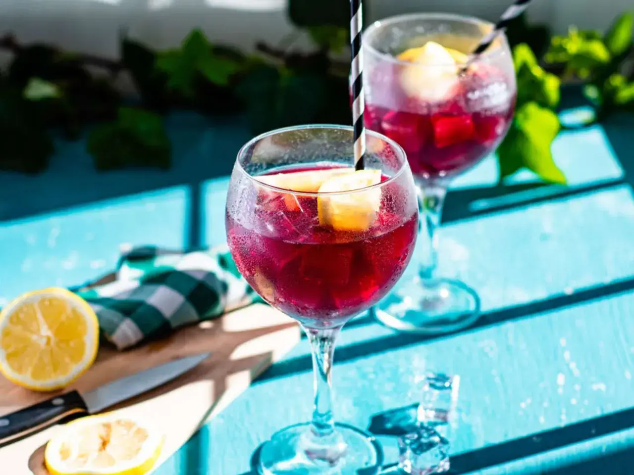 Två glas med tinto de verano, fyllda med is och citronklyftor, står på ett blått bord.
