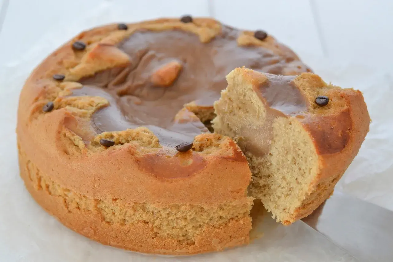 Torta al caffè ricette della nonna, soffice e profumata, con glassa al caramello e chicchi di caffè. Una fetta è già stata tagliata.