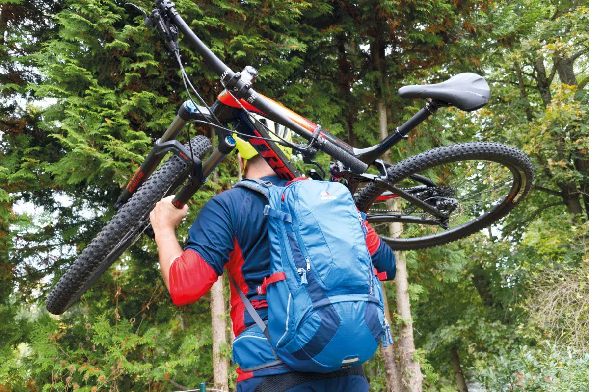 Mann mit Mountainbike und Deuter Trans Alpine 24 Rucksack im Wald.