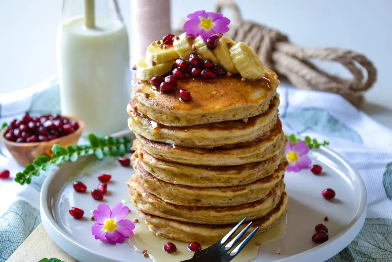 Pile de pancake banane avoine, garnie de fruits rouges, de rondelles de banane et de fleurs roses. Un délice matinal !