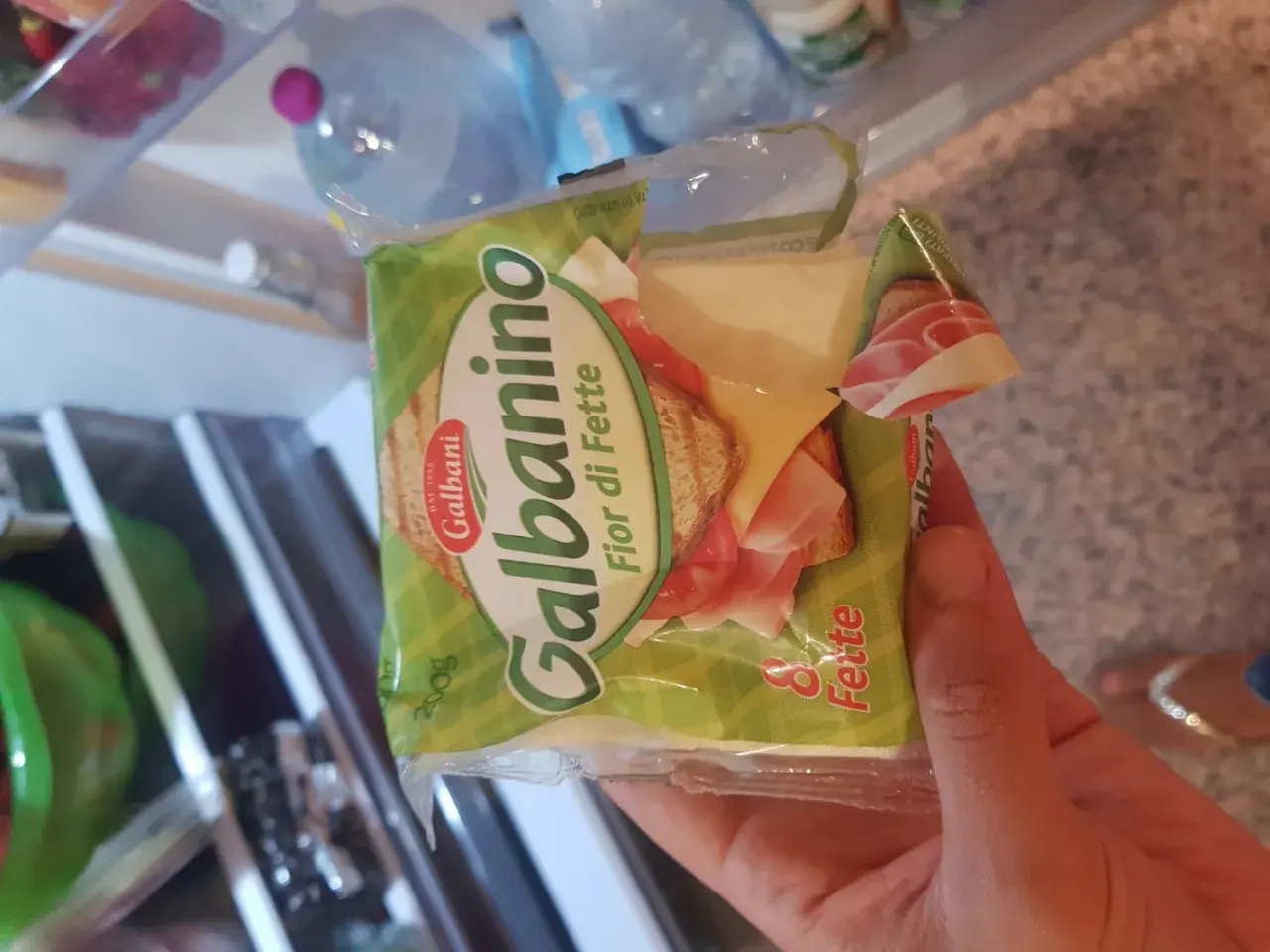 Una mano tiene una confezione di Galbanino Fior di Fette, con prosciutto e formaggio visibili. Perfetto per uno spuntino in gravidanza.