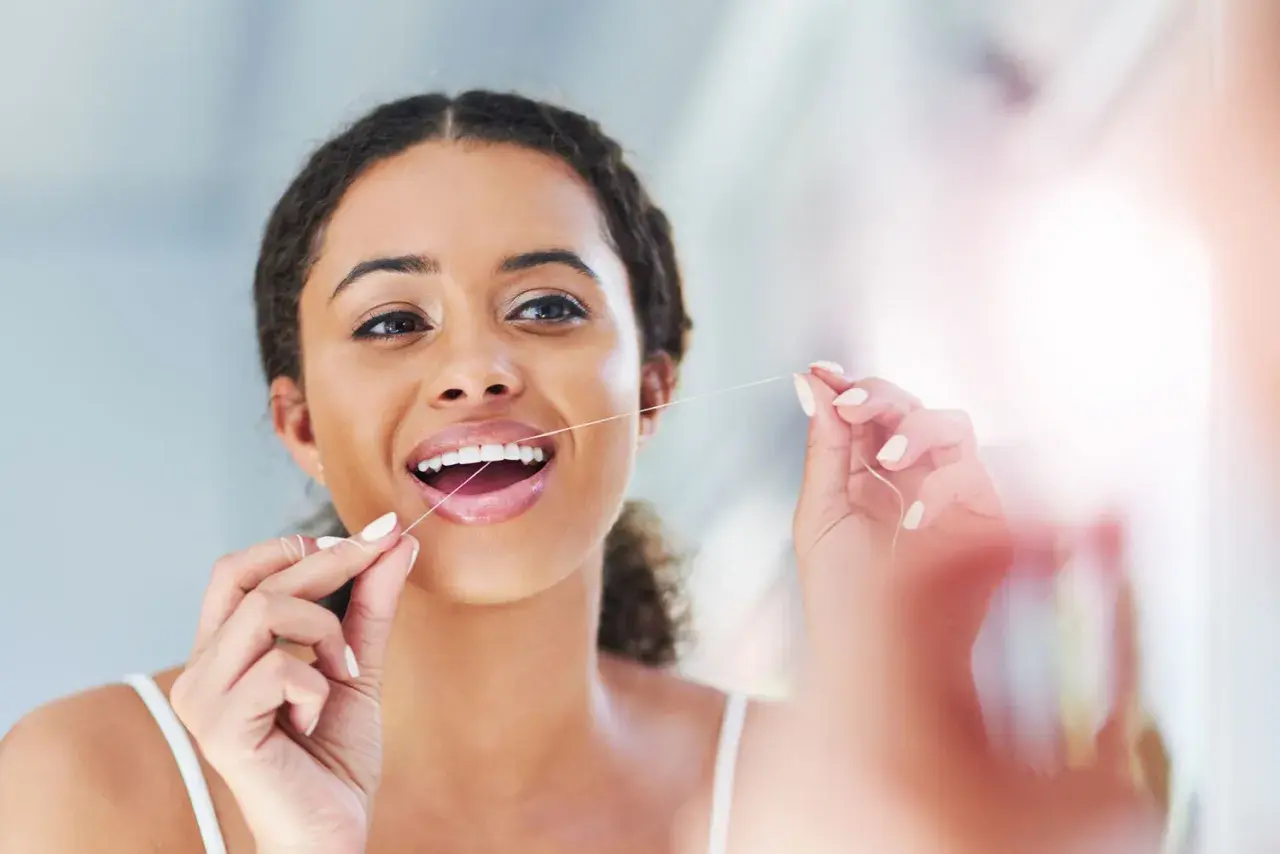 Donna sorridente usa il filo interdentale, un gesto quotidiano per un sorriso sano. Quante volte usare il filo interdentale? Almeno una volta al giorno.