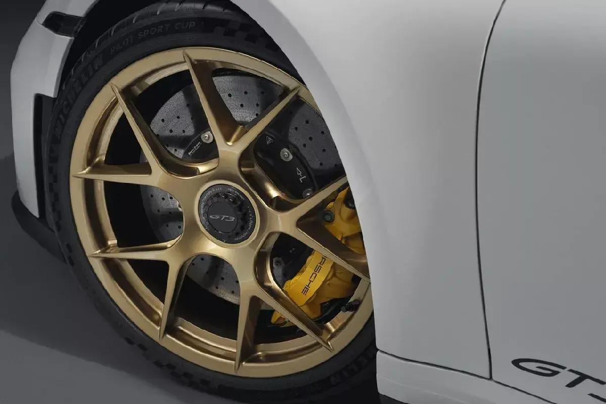 Detalle de un coche deportivo blanco con llantas doradas y pinzas amarillas. Se aprecian los discos de **frenos cerámicos** perforados, listos para la acción.