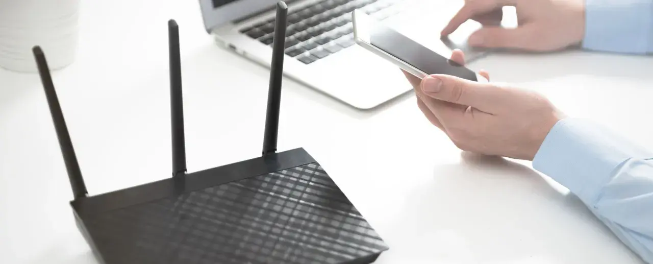 Osoba trzyma smartfon obok laptopa i routera, pokazując, jak udostępnić internet z telefonu na komputer przez USB.