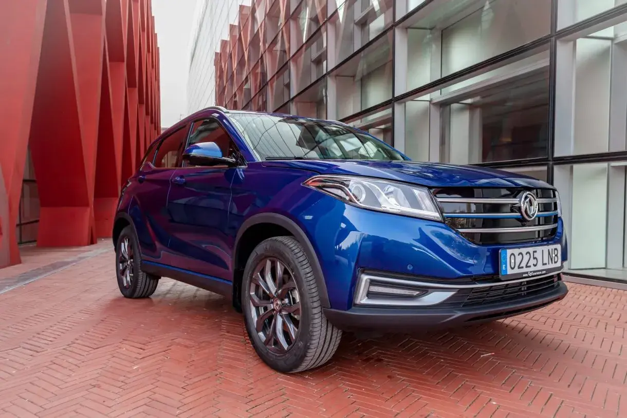 Niebieski SUV DFSK Seres 3 na tle nowoczesnej architektury.