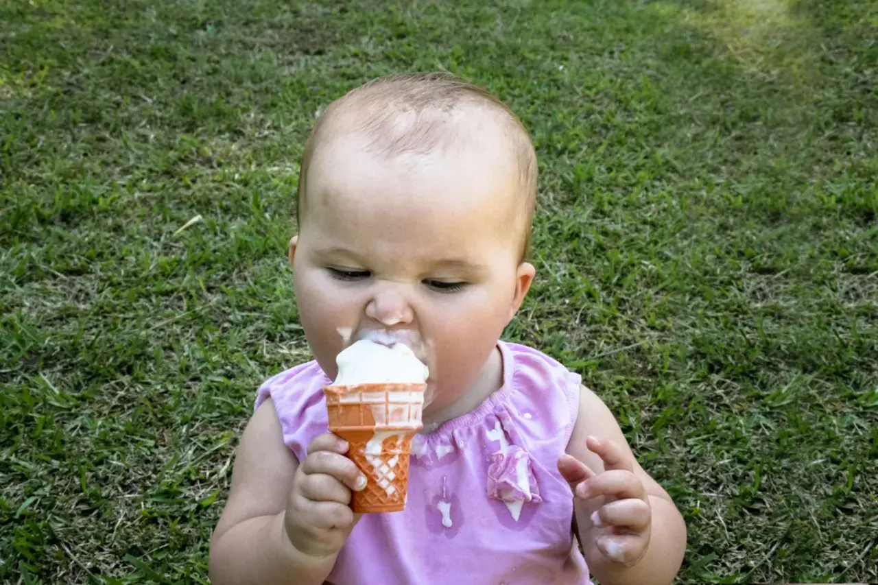 Kleines Baby mit Eiscreme im Gras. Ab wann Eis baby? Diese süße Erfahrung beginnt oft, wenn die Kleinen neugierig werden.