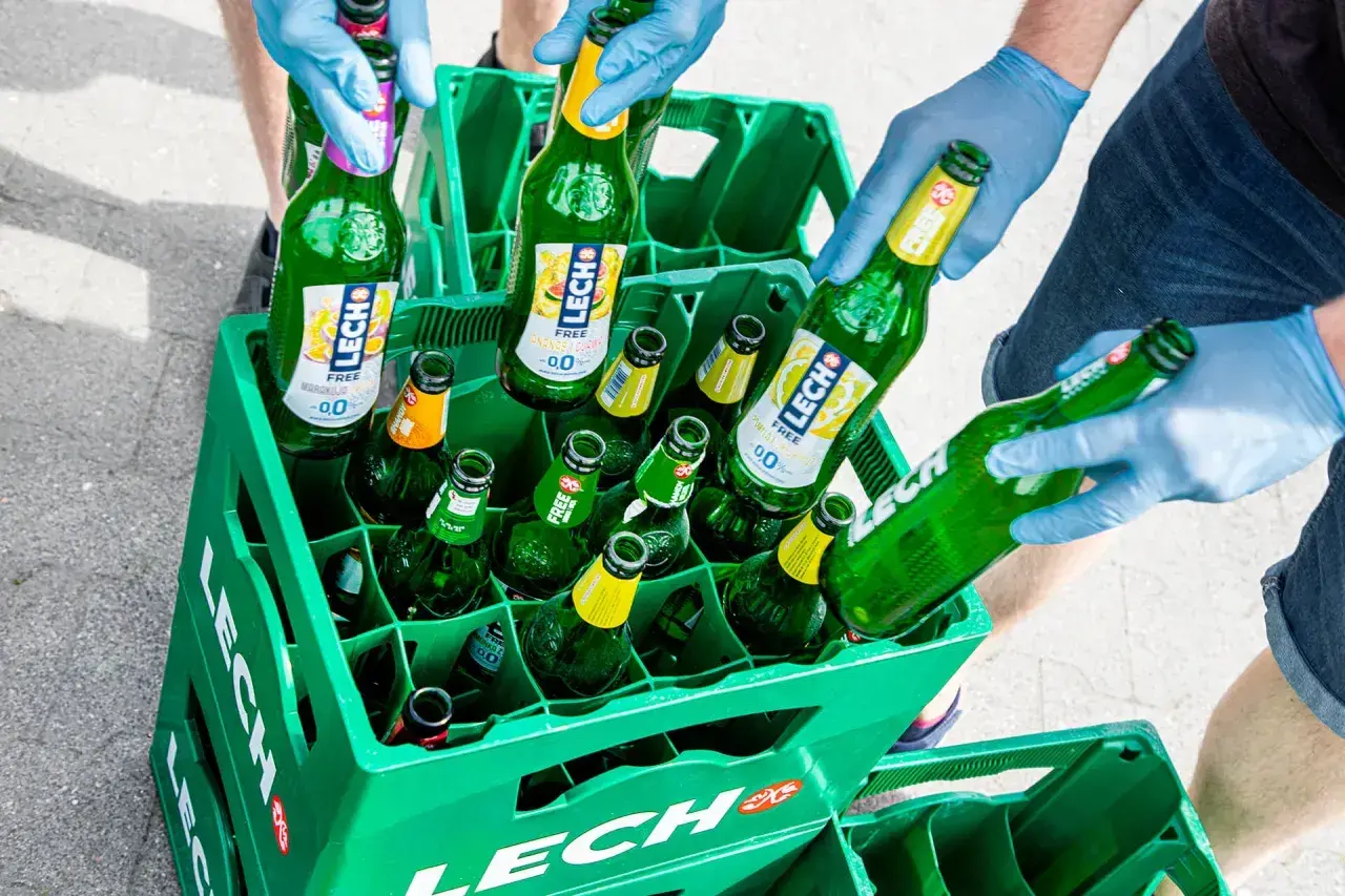 W zielonej kracie Lech Free jest 12 piw. Ręce w niebieskich rękawiczkach układają butelki.