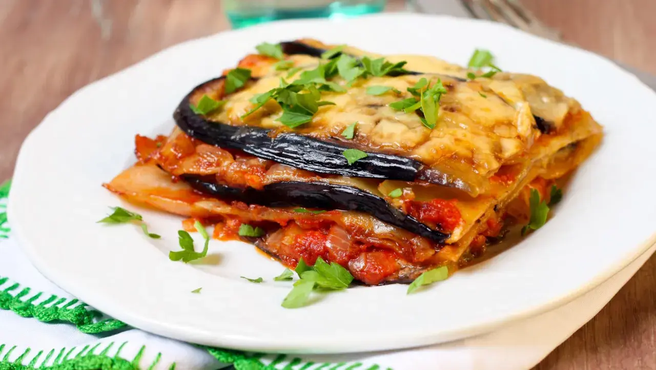 Deliciosa lasaña de berenjena, capas de berenjena, salsa de tomate y queso fundido, espolvoreada con perejil fresco.