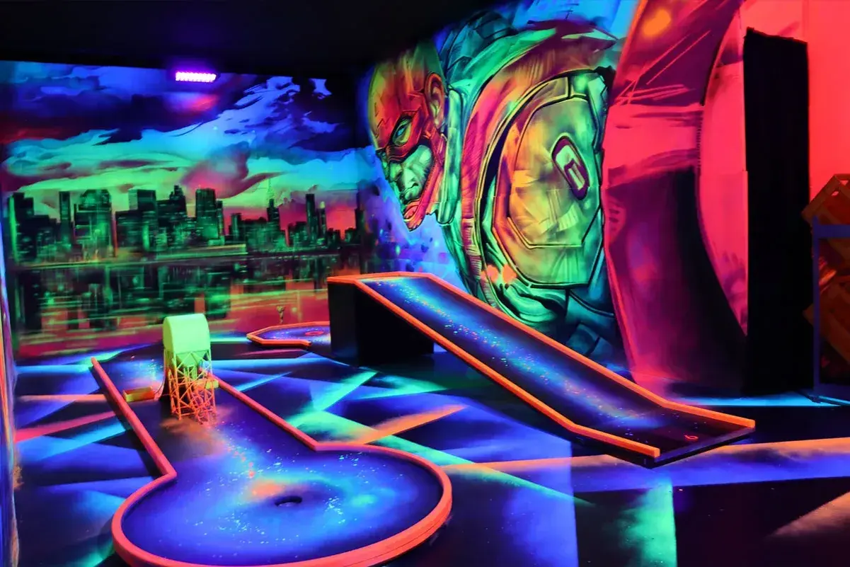 Neon-beleuchtete Bahnen und eine Skyline-Kulisse laden zum **Glow Minigolf** ein. Ein Superheld wacht über das Spiel.