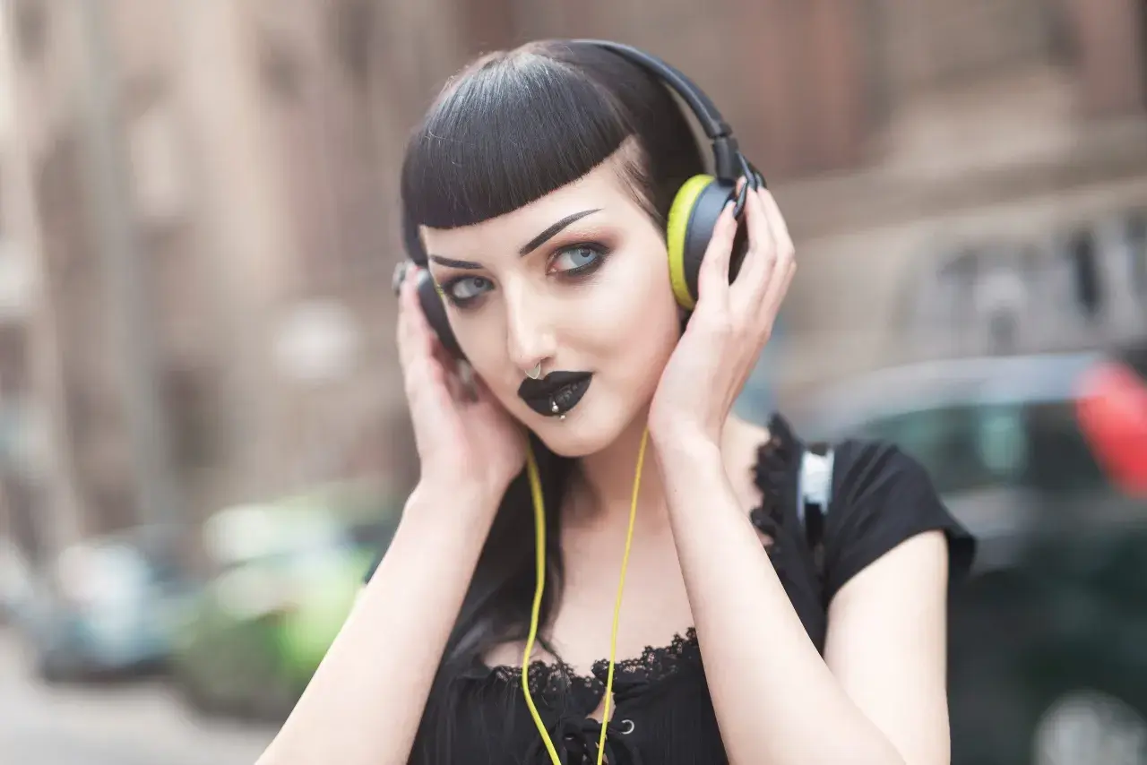 Mroczna goth girl w słuchawkach, z czarną szminką i kolczykiem w nosie, słucha muzyki na ulicy.
