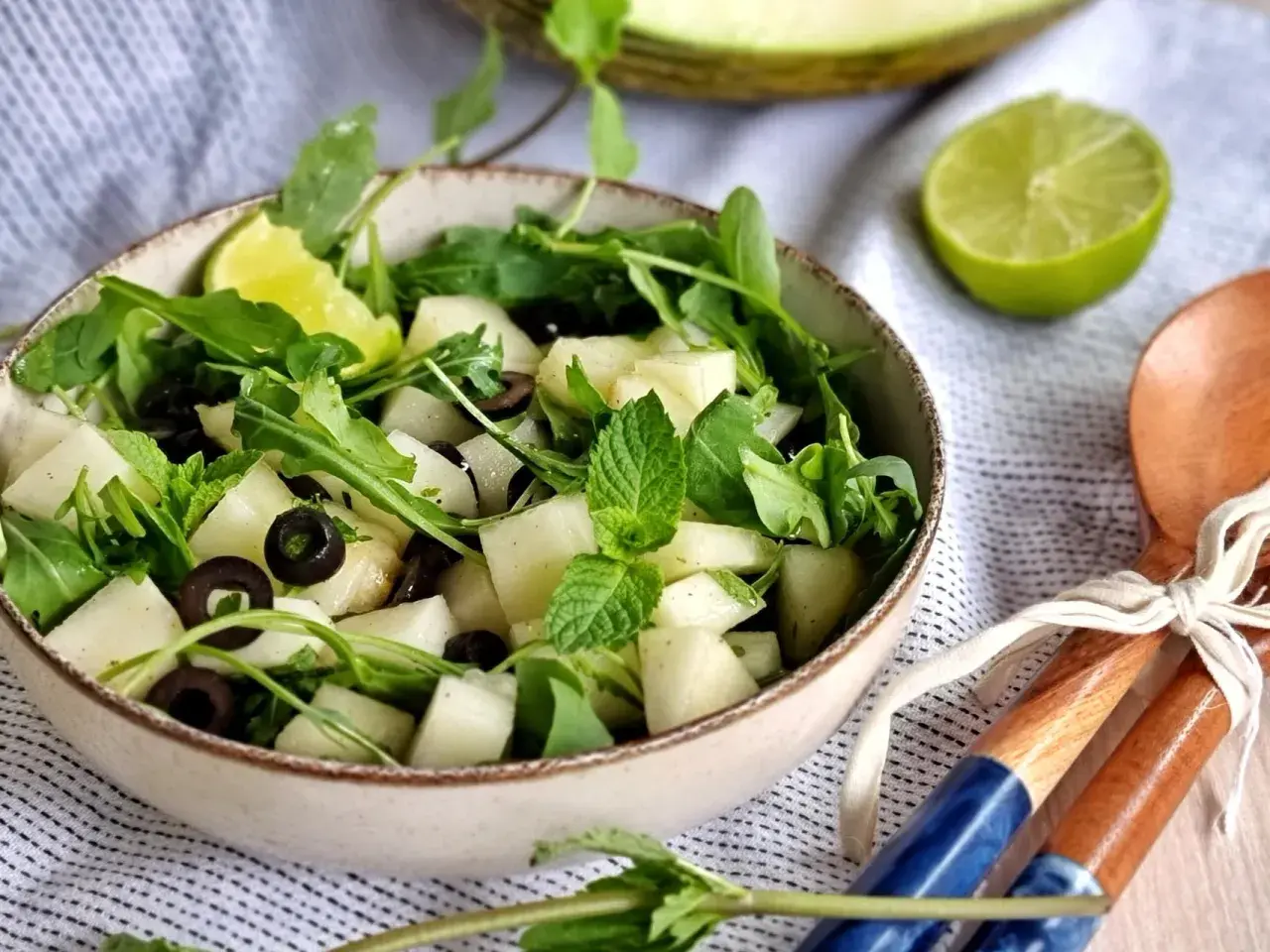 Refrescante ensalada de melón con rúcula, aceitunas negras y menta. Un toque de lima realza su sabor.