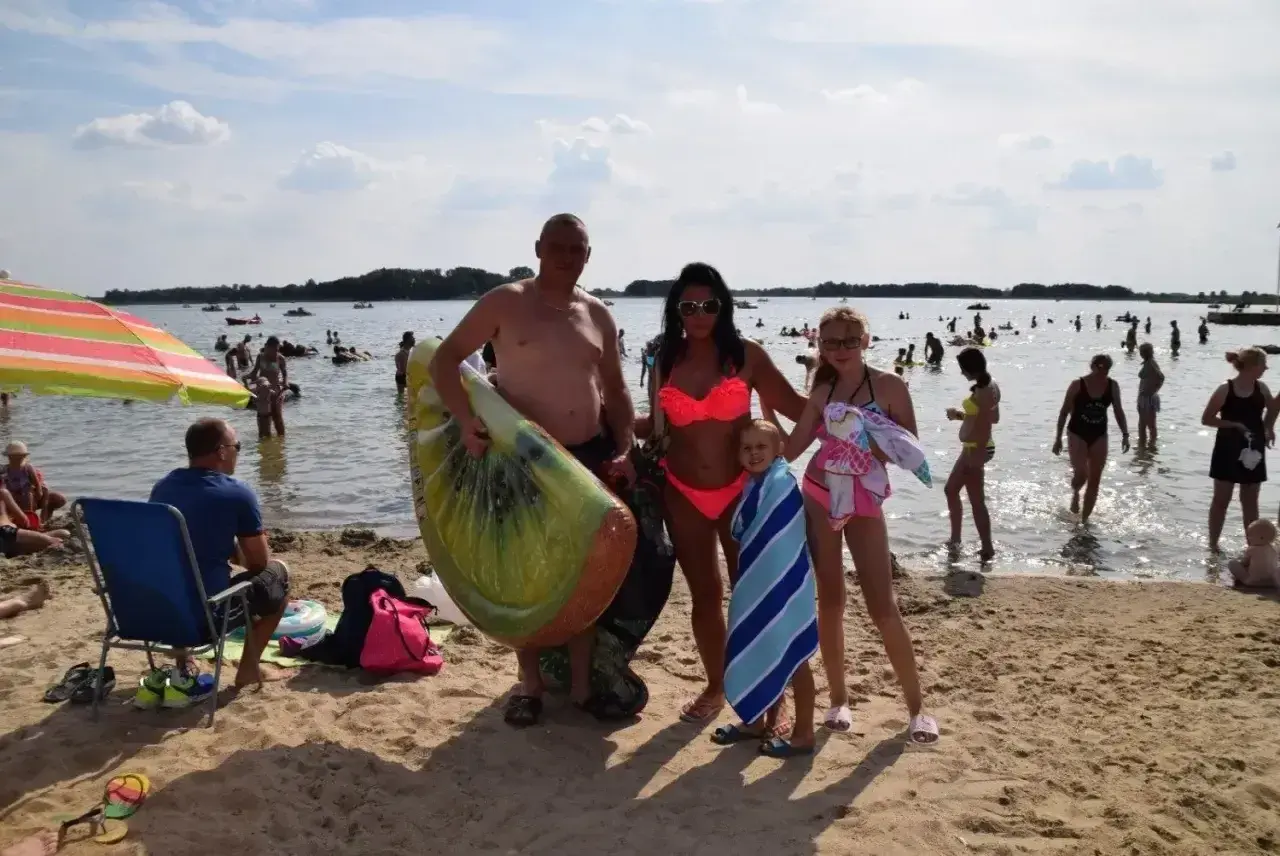 Rodzina na plaży nad jeziorem Niedzięgiel, z dmuchanym arbuzem i ręcznikami, cieszy się słonecznym dniem.