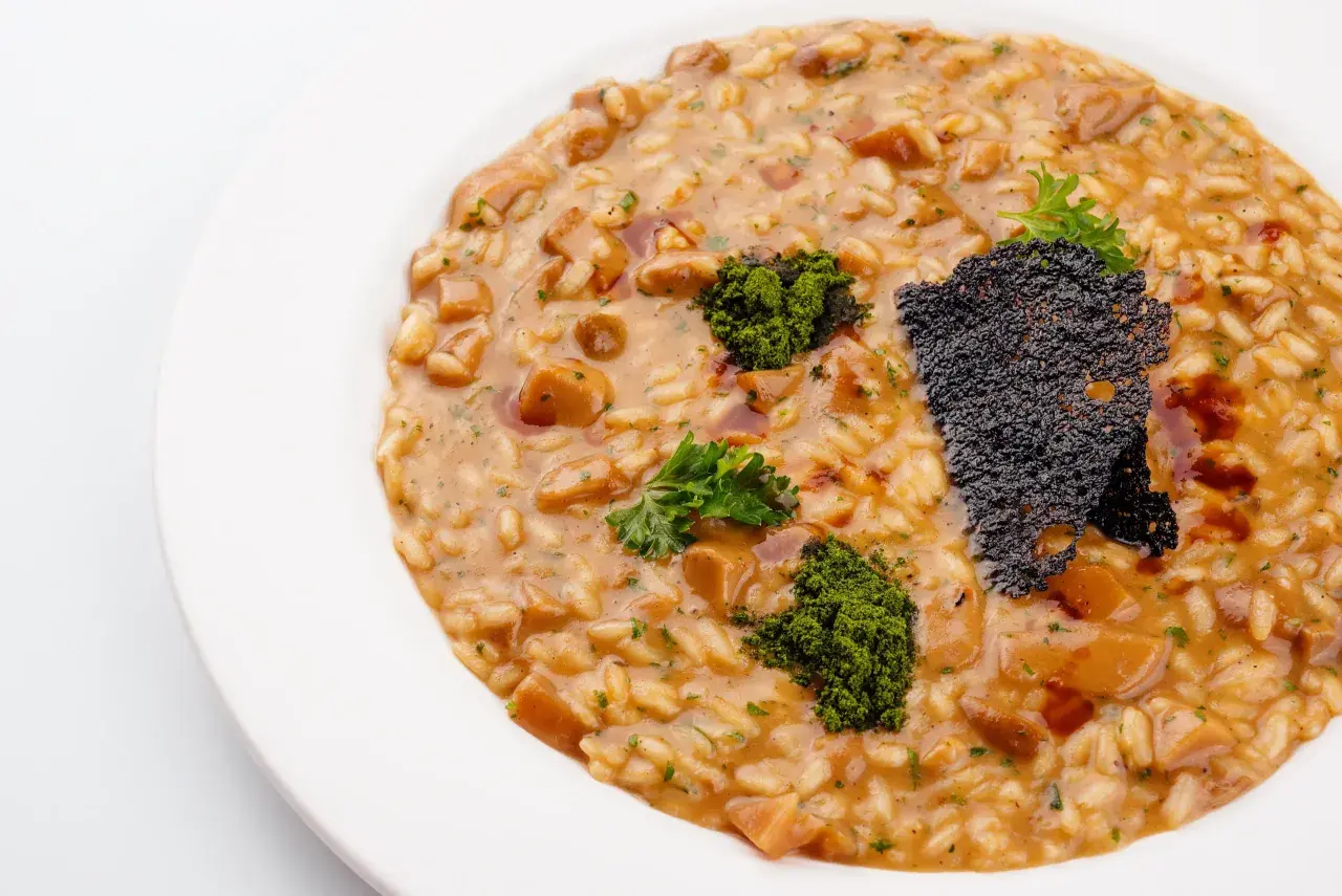 Risotto z grzybami i zieloną posypką na białym talerzu.