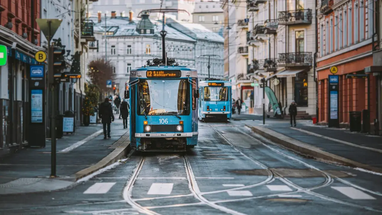 Niebieskie tramwaje na ulicy w Oslo, z budynkami po bokach.