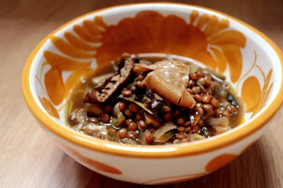 Un reconfortante plato de lentejas con boletus, servido en un cuenco decorado con motivos naranjas.