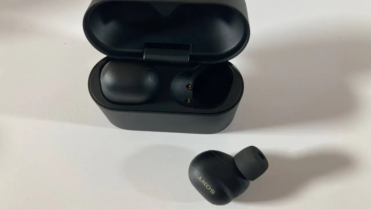 Schwarze Sony WF-1000XM6 Kopfhörer mit Ladecase. Ein Ohrhörer liegt daneben.