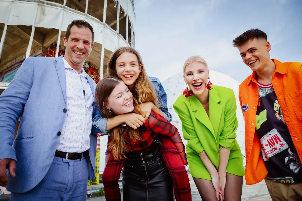 Eine fröhliche Familie genießt den Tag in Berlin. Vater, Mutter und drei Kinder lachen ausgelassen vor einer futuristischen Kulisse.