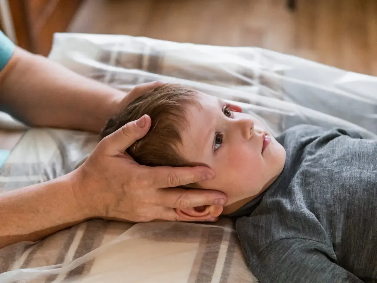 Chłopiec z obniżonym napięciem mięśniowym leży na plecach, a terapeuta delikatnie dotyka jego głowy.