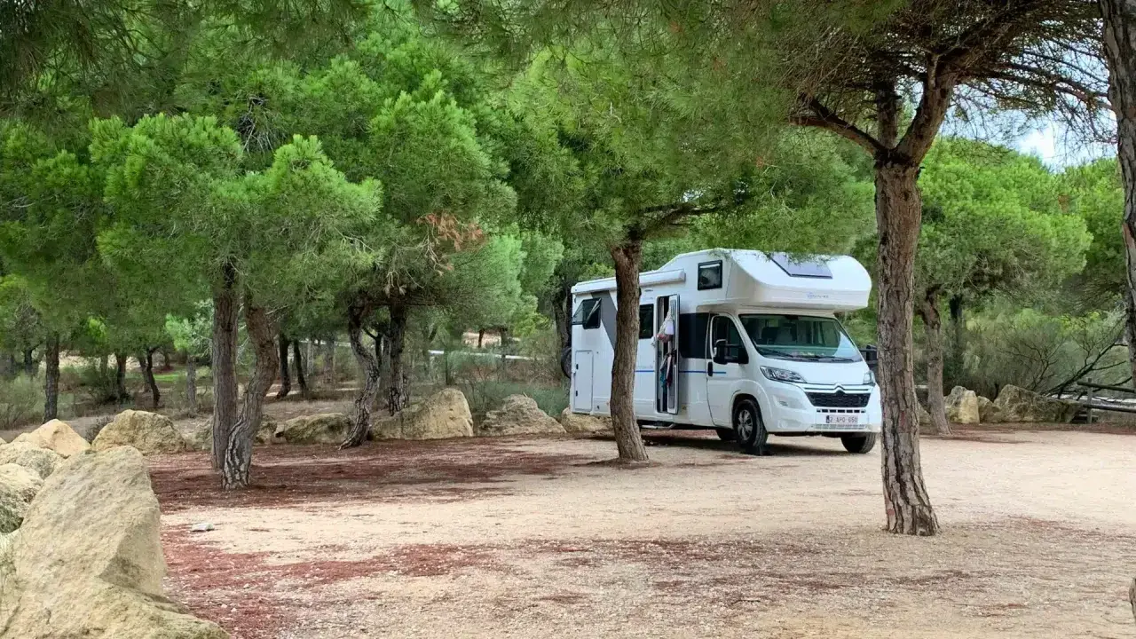 Un camping-car blanc est garé dans un endroit paisible, un spot camping-car sauvage, entouré de pins et de rochers.
