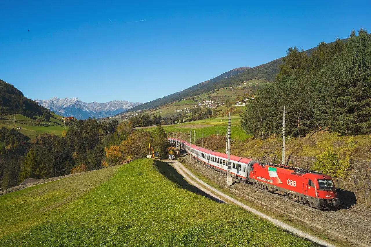 Roter ÖBB-Zug fährt durch eine grüne Alpenlandschaft. Die Strecke von Ljubljana nach Zagreb ist malerisch.